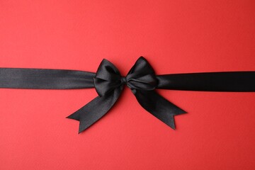 Black satin ribbon with bow on red background, top view