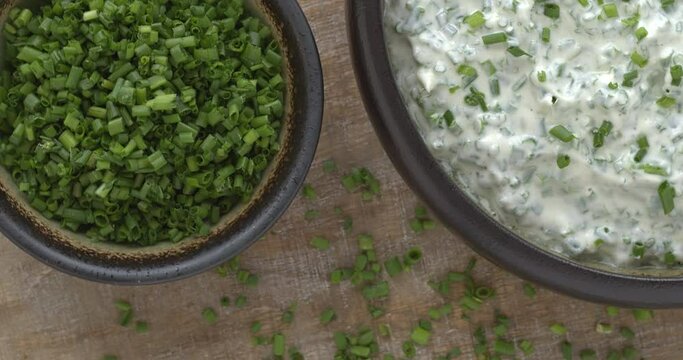 Homemade Greek Yogurt Chive dip in a clay bowl. A second bowl with chopped chives and garlic cloves on the side. Table spin. 