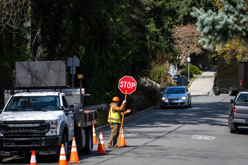 City workman with temporary stop sign managing traffic around large work truck in in street with...