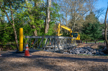 New foot bridge construction installation at suburban public park with excavator and caution tape