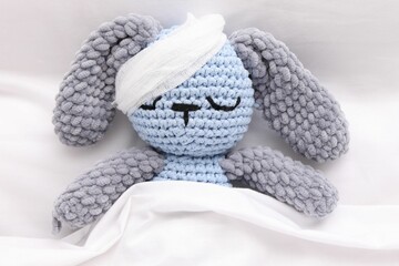 Toy cute bunny with bandage under blanket in bed