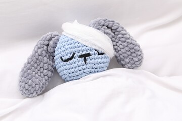 Toy cute bunny with bandage under blanket in bed