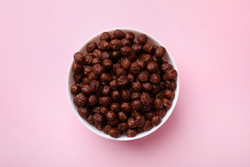 Chocolate cereal balls in bowl on pink table, top view