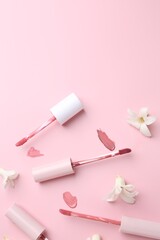 Different lip glosses, applicators and flowers on pink background, flat lay. Space for text