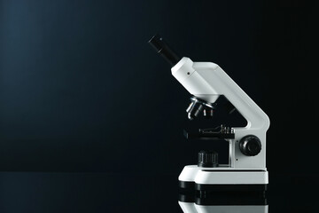 Modern microscope on black mirror surface, space for text