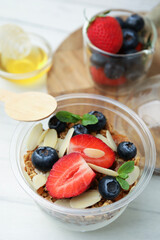 Tasty granola with berries, yogurt and almond flakes in plastic cup on white table, closeup