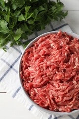 Raw ground meat in bowl and parsley on table, top view