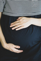 Asian pregnant hand touching belly softly in close, dark dressing and vertical frame