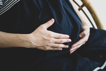 Closeup of Asian pregnant hand touching belly softly with dark dressing on wood chair, side view