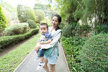 Smiling asian mother and son standing in lush garden and day