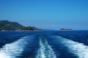 瀬戸内海を航行する定期船の航跡と島の風景。