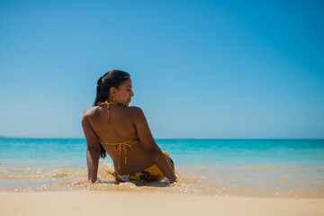 joven hispano latina al aire libre sentada en la playa en bikini tomando el sol en vacaciones 