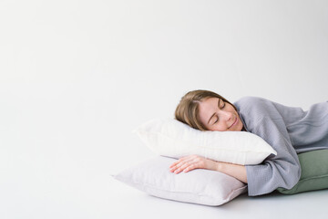 A woman lies comfortably on her side, embracing a white pillow with a tranquil expression. She is...