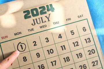 Hand pointing on July 1 2024 date on calendar flat lay in blue background. Canada day celebration...