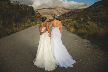 dos mujeres caminando por la calle principal usando sus vestidos de boda al aire libre  - obrazy, fototapety, plakaty