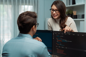 Woman colleague standing opposite to man programmer working on desk to discuss coding website...