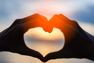 Couple doing heart shape with their hands on shore and love sign background