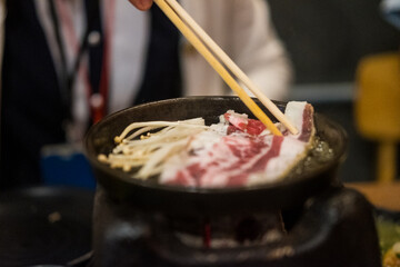 Hand using wood chopsticks grilled meat in hot pan. Close up
