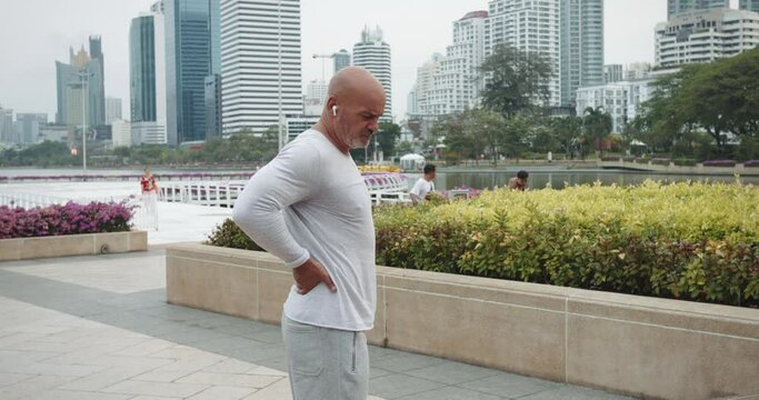 After workout public park man in pain clutching back discomfort back injury. Male winces agony back throbbing with aftermath workout gone awry Person grimace pain back injury after session exercise.