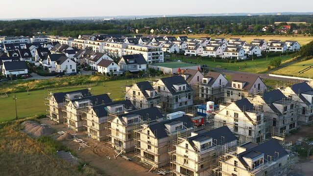 Overflight of a housing estate with many modern detached houses and apartment buildings and a building site with detached houses under construction in a rural area.