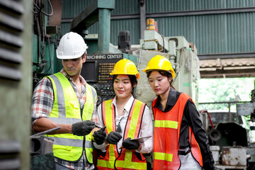 Group of male and female industrial engineer workers with helmet and safety vest inspecting engine at manufacturing plant industry factory. Worker working with machinery machine in industry workplace.