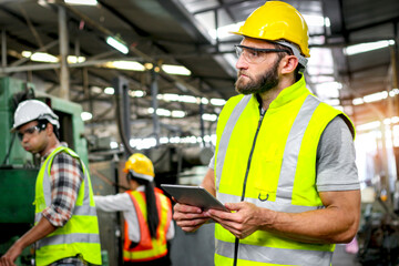 Industrial engineer with helmet and safety vest holds tablet for checking process and machinery...