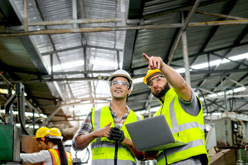 Industrial foreman and worker with helmet and safety vest using laptop computer during discussing...