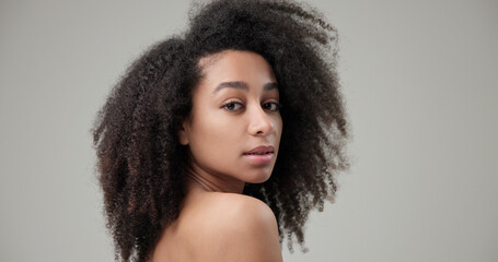 Beauty and Healthcare concept - Beautiful African American woman with curly afro hairstyle hair and clean, healthy skin on gray studio background posing and looking at camera