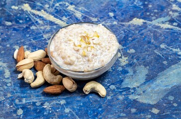 Cracked Wheat Kheer or Payesh Garnished with Cashew, Pistachio, Almond in a Glass Bowl Isolate on Blue Wooden Background with Copy Space, Also Known as Ksheeram, Milk Pudding