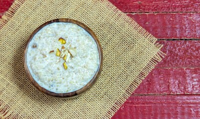 Top View of Cracked Wheat Kheer or Payesh Garnished with Cashew, Almond, Pistachio in a Wooden Bowl Isolate on Red Wooden Background with Copy Space, Also Known as Ksheeram, Milk Pudding