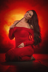 Young beautiful girl with dark hair and in the red dress posing in the dark background with the...