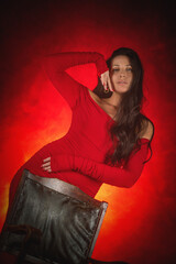 Young beautiful girl with dark hair and in the red dress posing in the dark background.