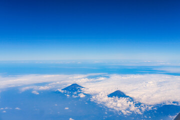 Aerial view from a plane over Java Island, showcasing majestic mountains rising through a sea of clouds under a clear blue sky