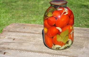 tomatoes in a jar. large glass jar of canned tomatoes on an old wooden table.blurred background. natural farm products concept. homemade canning