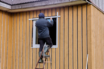 Construction worker installs external slopes on window of wooden rural house from facade.