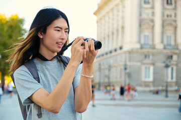 Asian male tourist smiling and taking photos with a camera while sightseeing in Madrid, Spain.