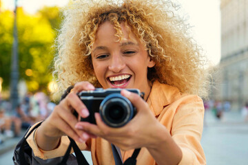 Happy Latin female tourist laughing and taking photos with a camera while sightseeing in Madrid, Spain.