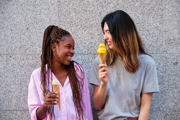 Two multiracial happy friends with ice creams laughing in summer at street.
