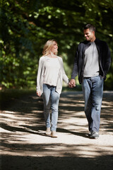 Obraz premium Couple, holding hands and walk in park with love on date for relationship and bonding with smile. People, walking and outdoor with happiness in nature with partnership, conversation and care