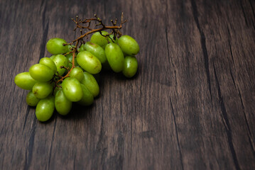 Comida. Ramillo de uvas verdes sobre mesa de madera.