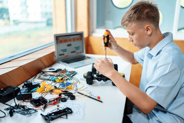 Blonde hair schoolboy using screwdriver fixing robotics vehicle learning technology in STEM class....