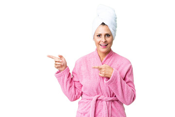 Middle age caucasian woman in a bathrobe over isolated background surprised and pointing side