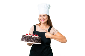 Middle age pastry chef woman holding a big cake over isolated background giving a thumbs up gesture