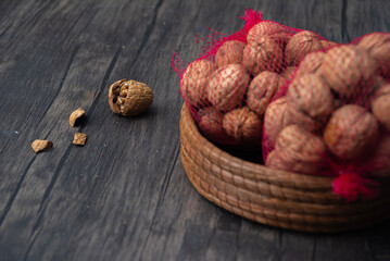 Comida. Red roja rota llena de nueces sobre pequeña canasta, con una nuez abierta sobre mesa de...