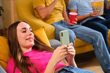 Young Caucasian woman using her smartphone laying on the sofa at shared student flat.