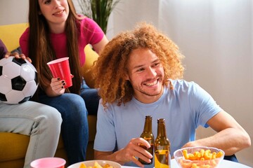 Young Hispanic man watching soccer match with friends at shared student flat.