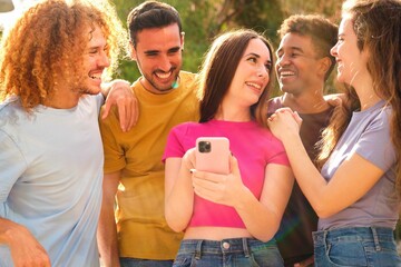 Group of young teenagers watching something funny on mobile screen at street.