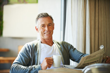 Mature, man and newspaper for reading in home, relax and information or articles in morning with coffee. News, breakfast table and rest and calm for entertainment pages, current events in apartment