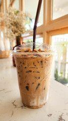 Iced cappuccino coffee in a clear take-home cup. There are dried flowers in the background.