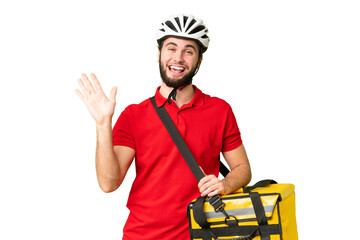 Young delivery man with thermal backpack over isolated chroma key background saluting with hand...